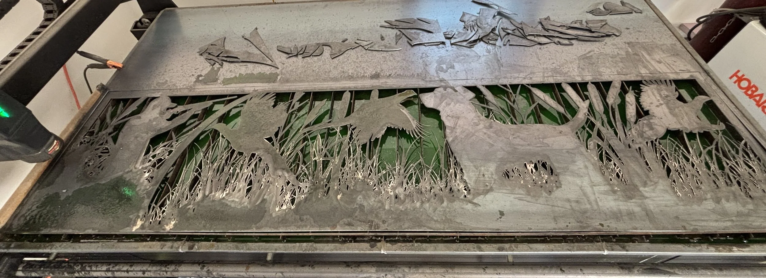 Metal sheet with intricate cut-out dinosaur and prehistoric plant designs in progress, placed on a worktable.