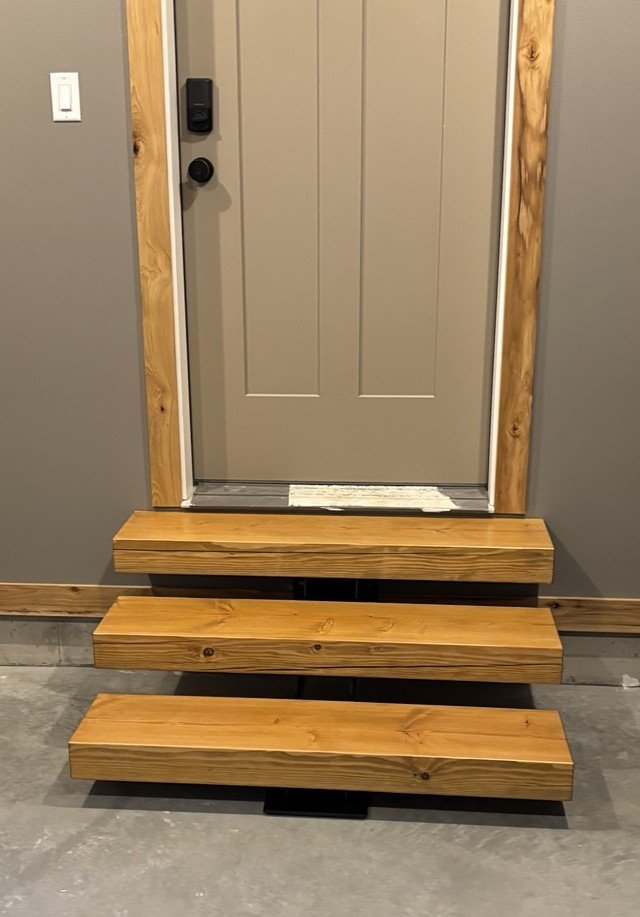 Wooden stairs leading to a front door, with a small step at the entryway.