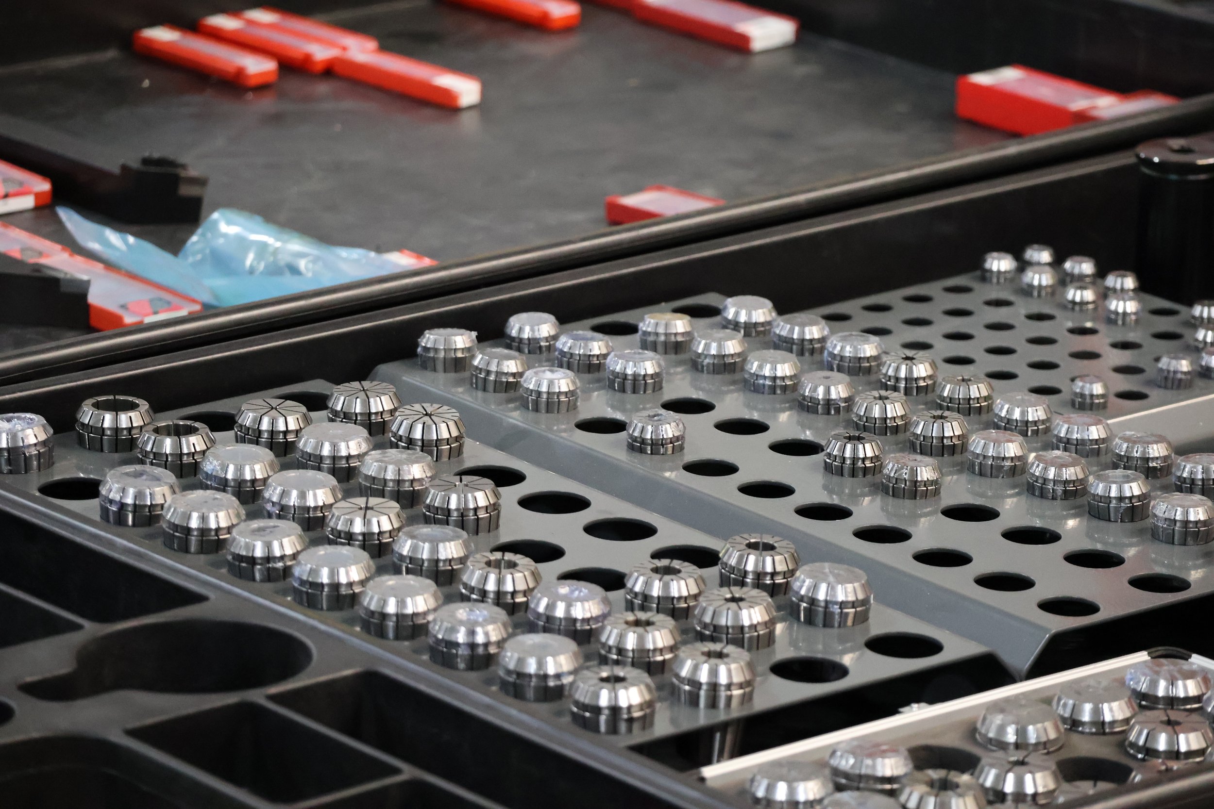 Assorted metalary tooling pieces arranged in storage cases, with some blue packaging in the background.
