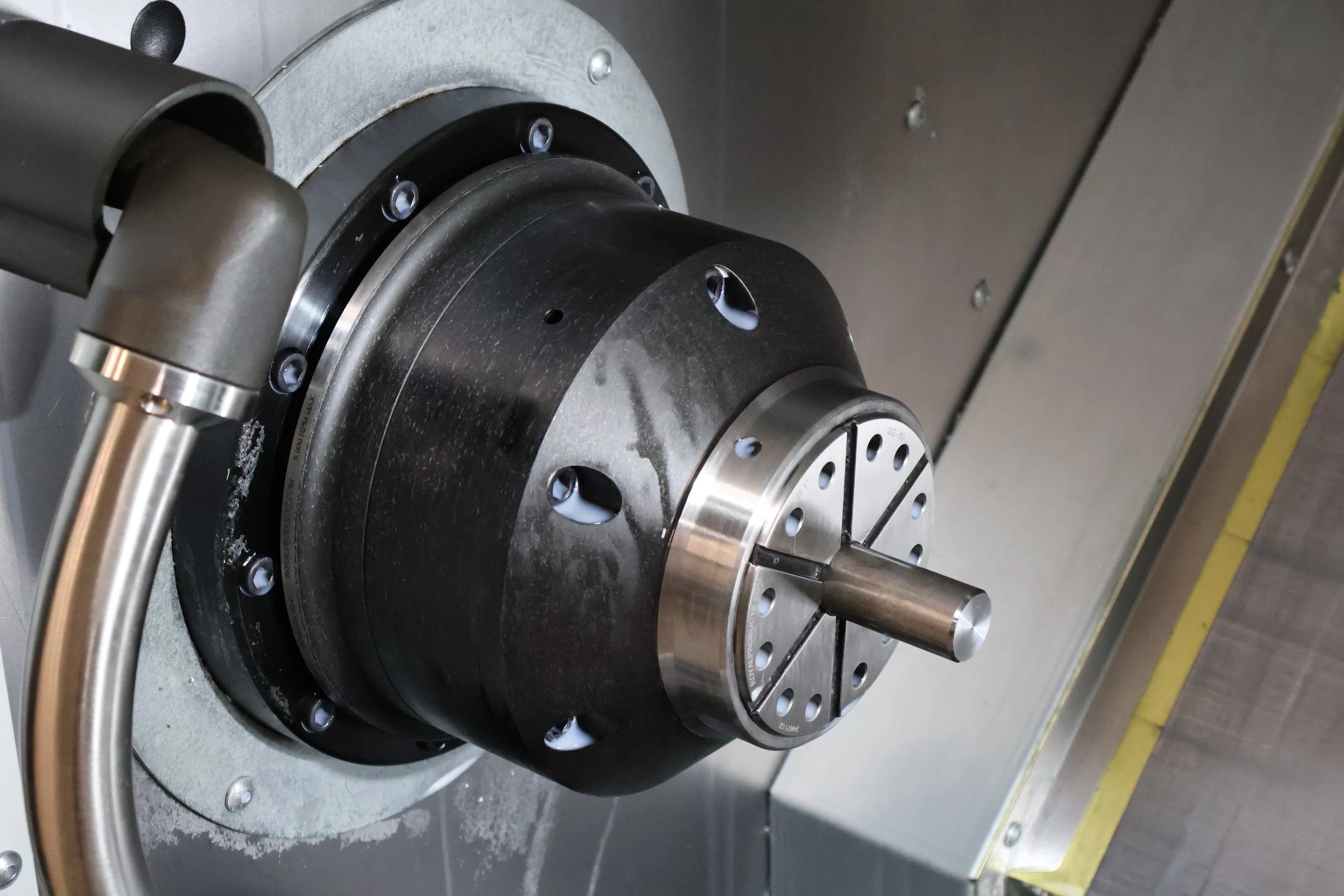 Close-up of a CNC machine spindle with a metallic drill chuck attached, mounted on a metal surface.