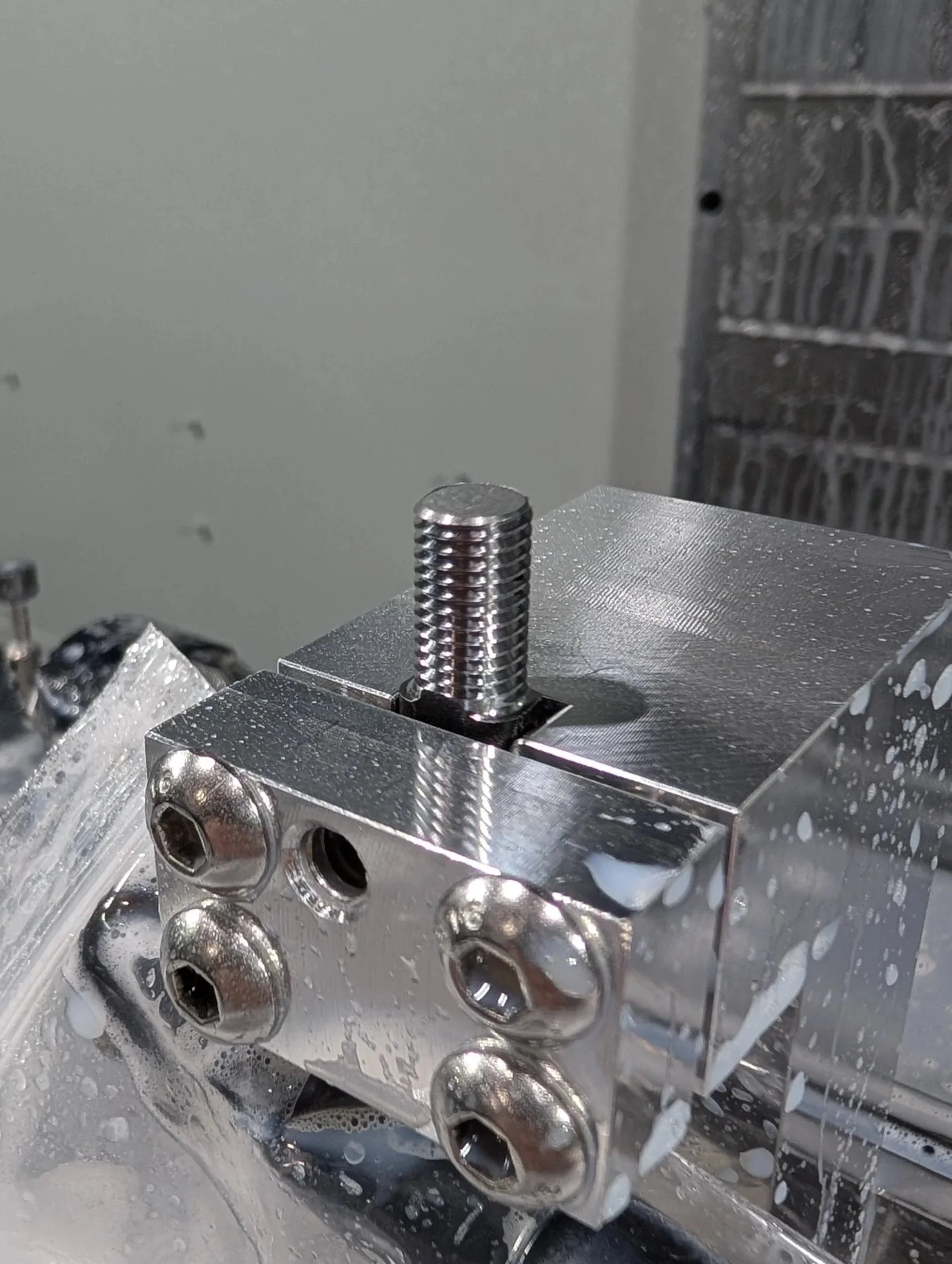 Close-up of a metal machine component with a threaded bolt and several screws, with some liquid on the surface.