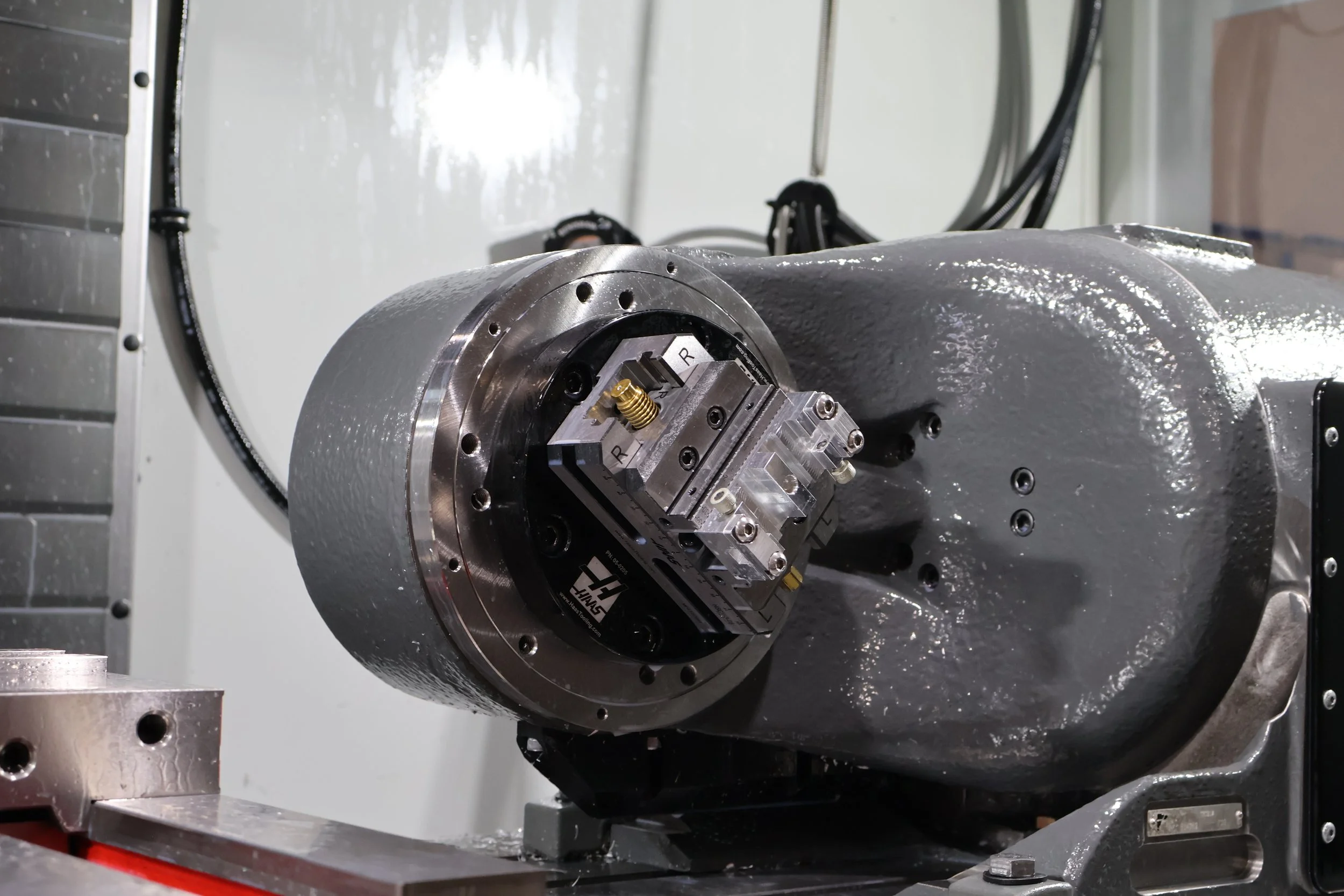 Close-up of a grey industrial robotic arm with a mounted precision tool or sensor, attached to a rotation joint, in manufacturing or laboratory setting.