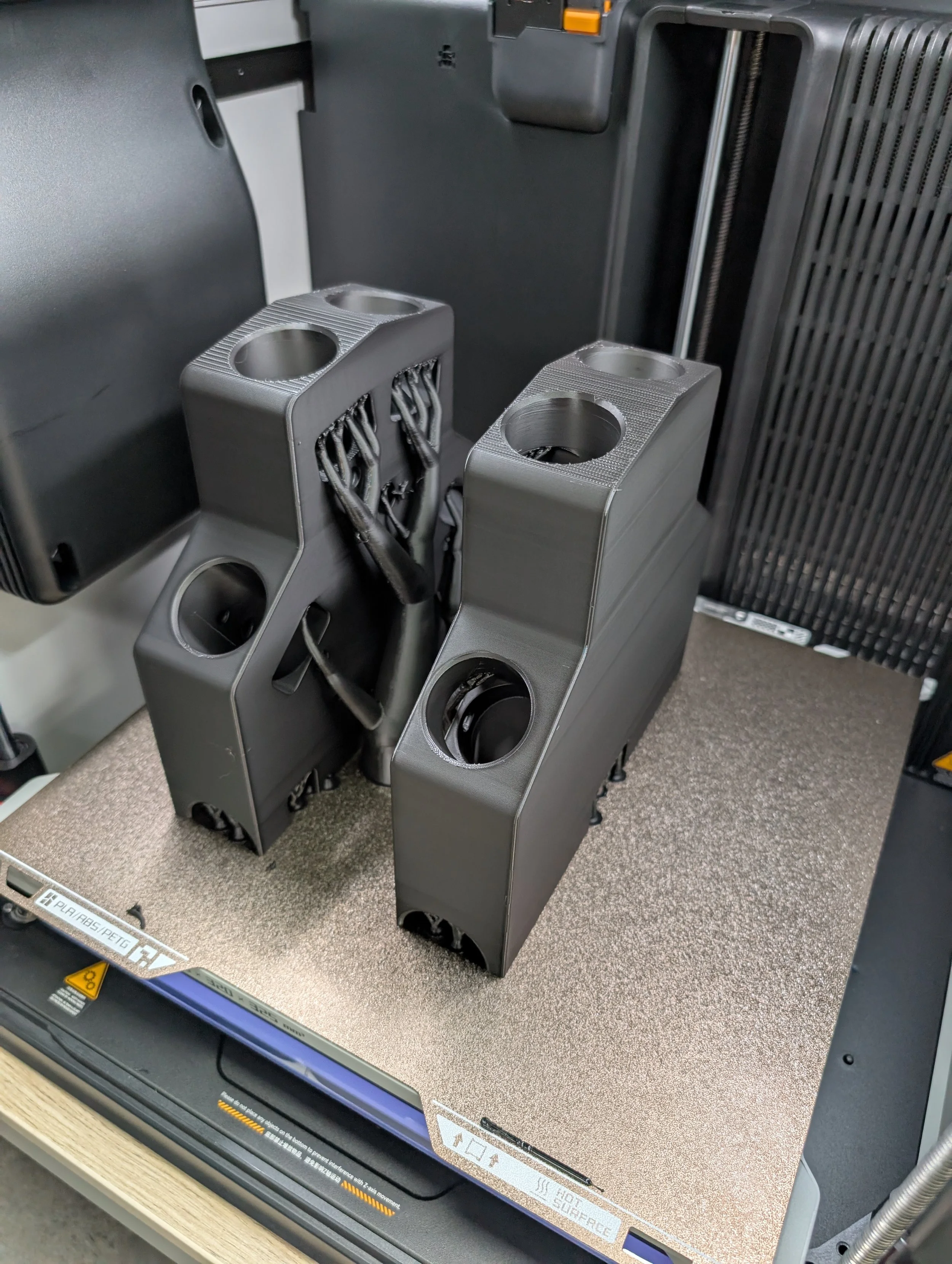 3D printed black parts with cylindrical holes and wires on a 3D printer bed.