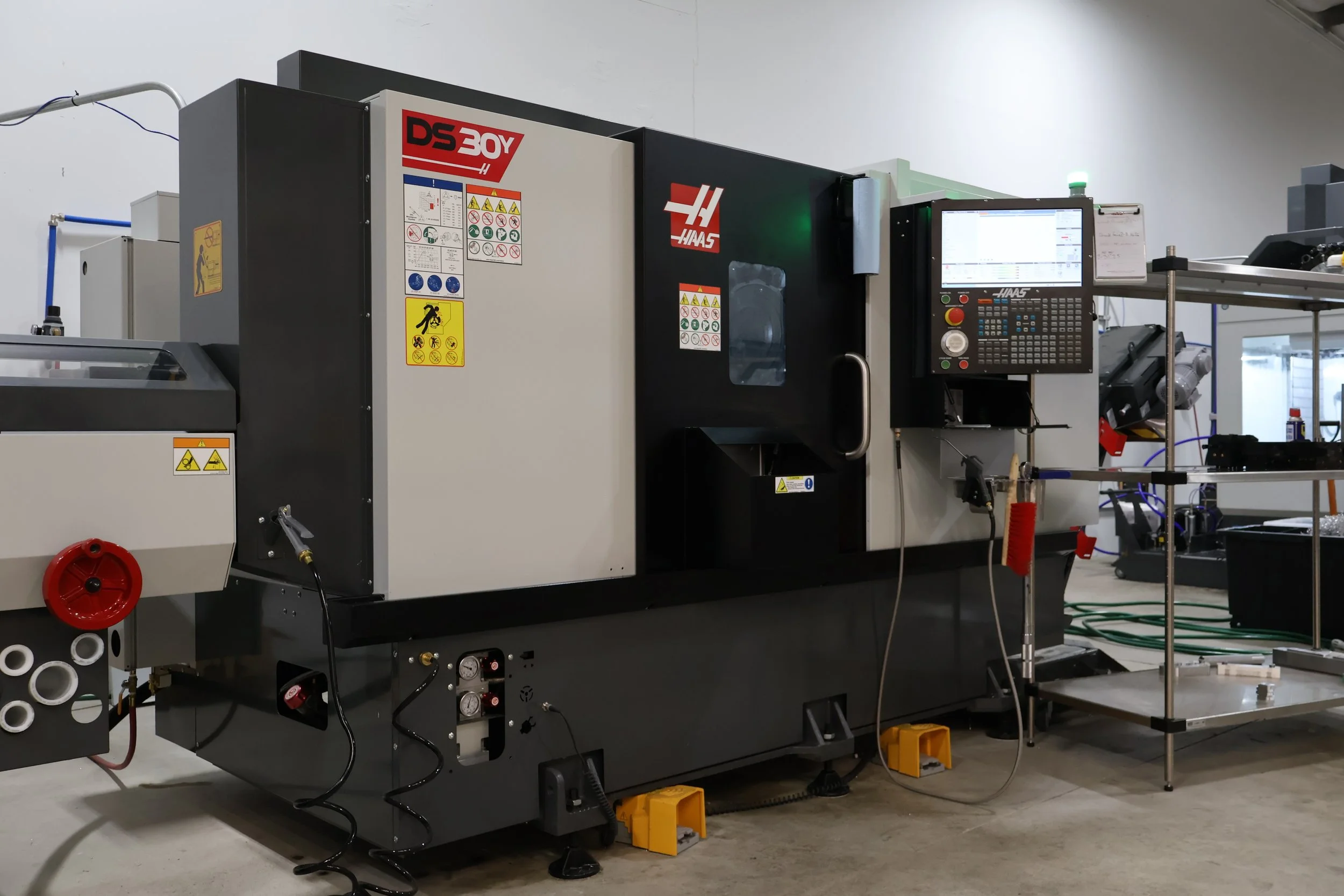 A CNC machine labeled Haas DS 30Y in a workshop with control panel and safety signs.