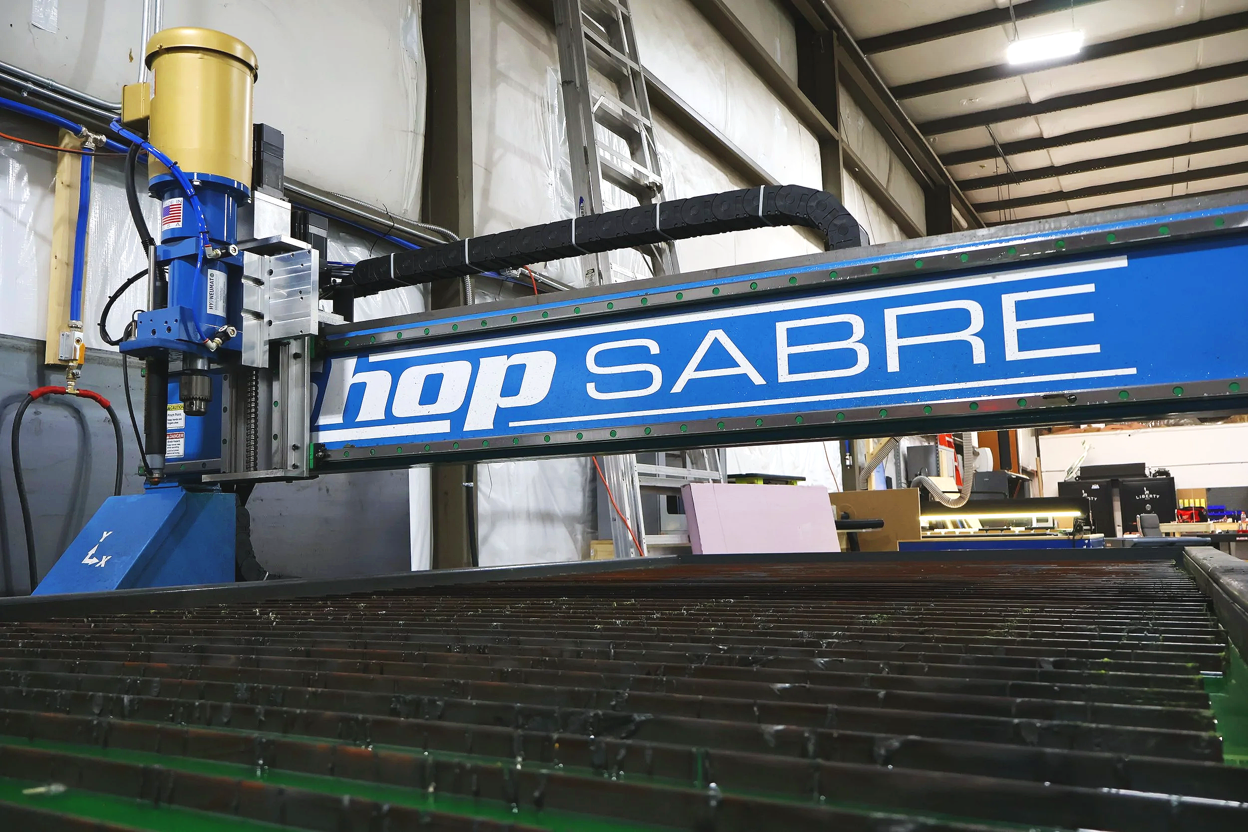 Industrial laser cutting machine in a workshop with the words "shop SABRE" on the blue beam.
