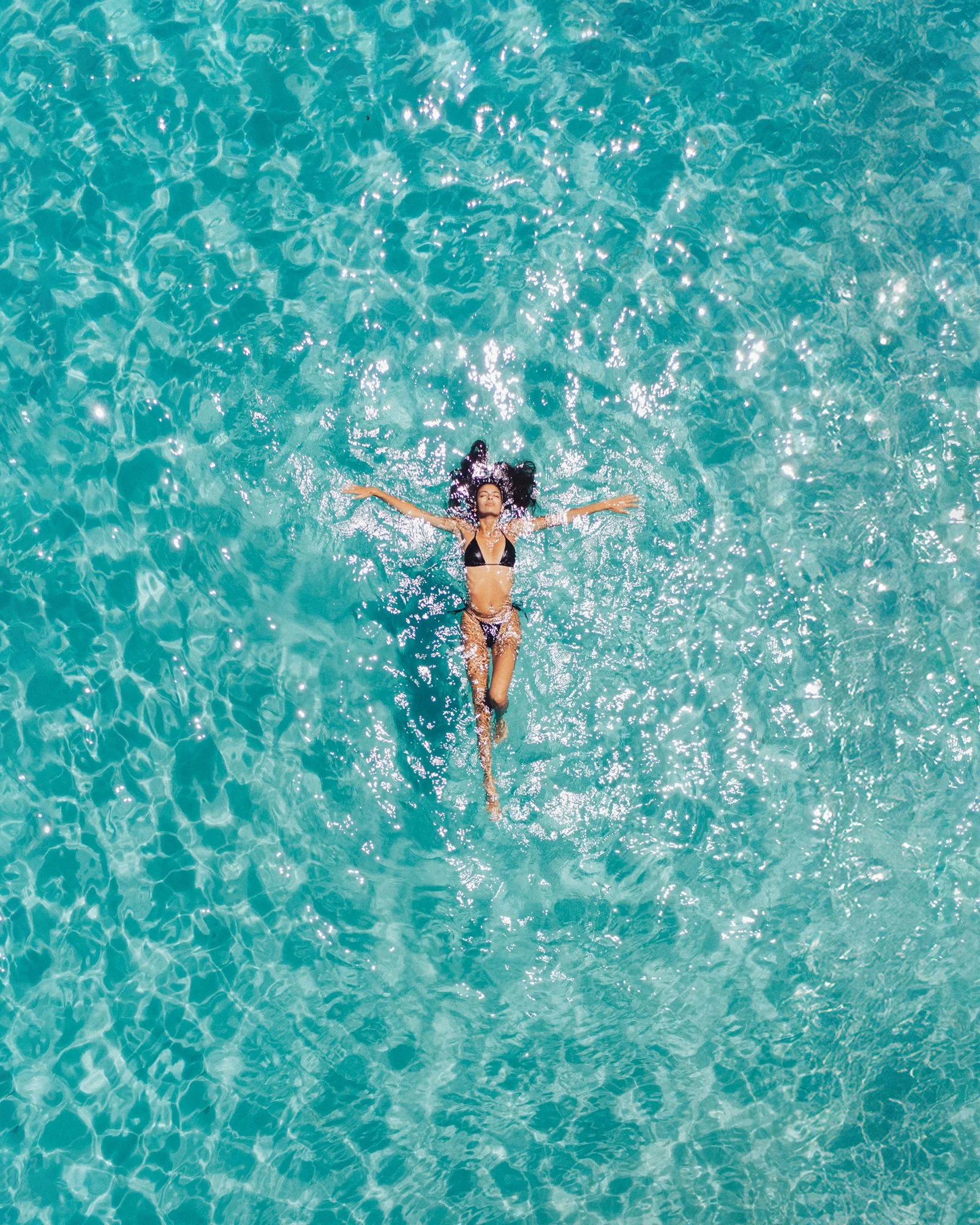 Donna in bikini nero che galleggia in una piscina azzurra
