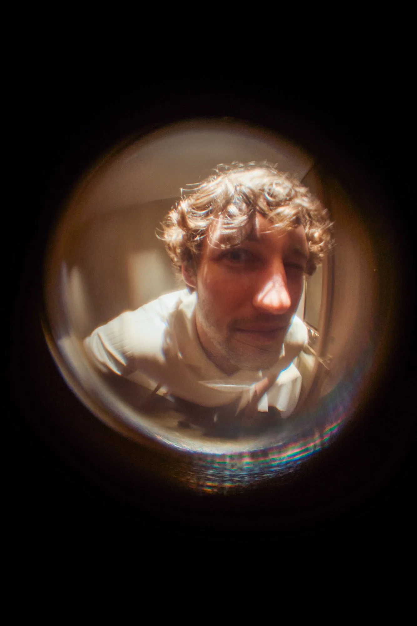 Ragazzo con capelli ricci, vestito con una maglietta bianca, scattando una foto con un dispositivo che crea un effetto a cavallo dell'immagine e sfocatura a bulb.
