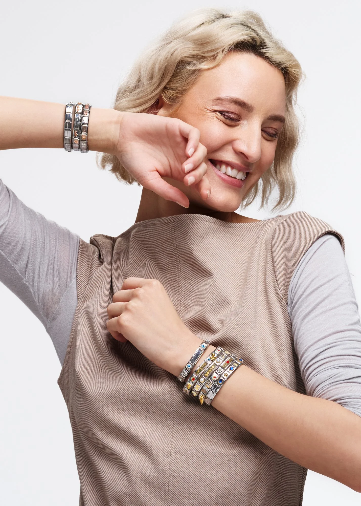 Una donna sorridente che si tocca il viso con una mano, indossa diversi braccialetti colorati e un vestito beige.