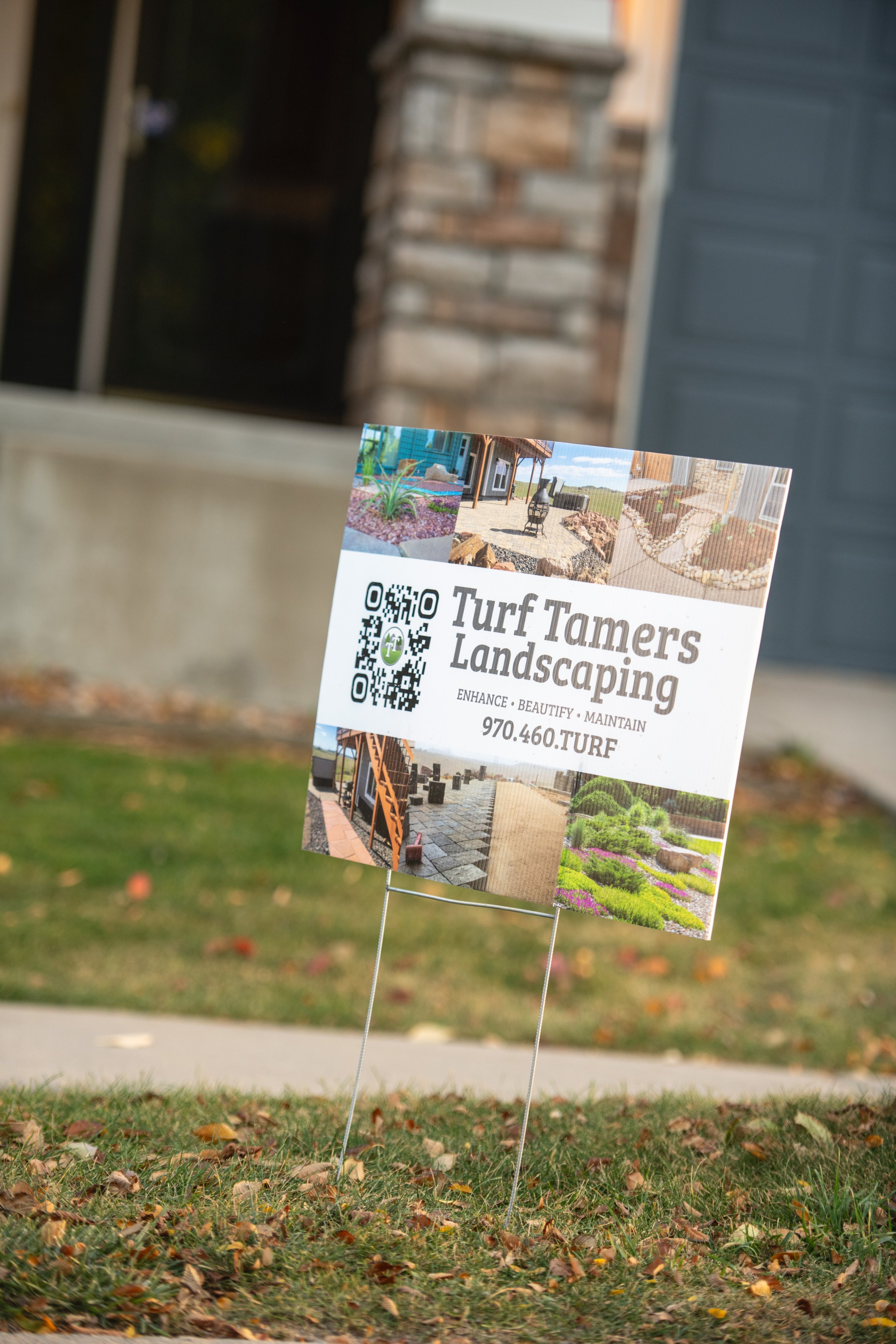 Sign for Turf Tamers Landscaping with pictures of landscaped yards, QR code, and contact information in a residential yard