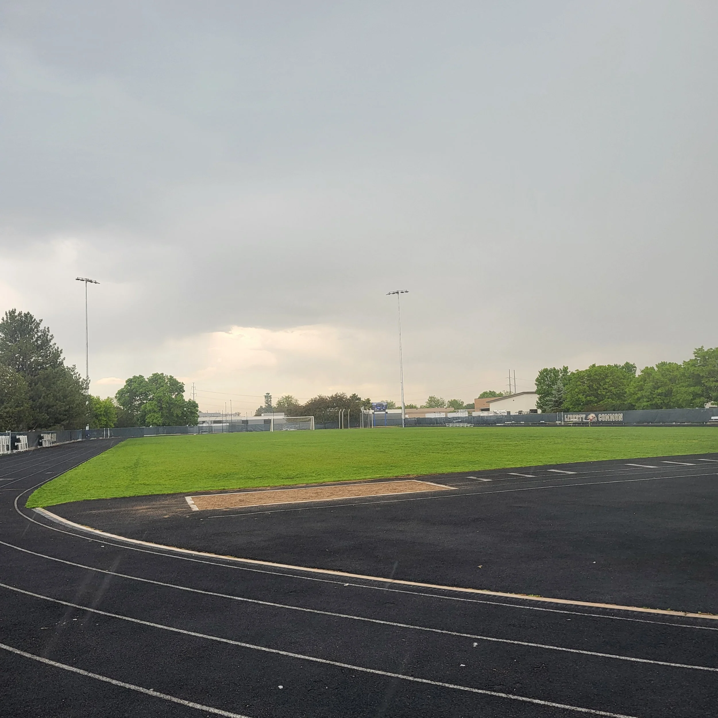An outdoor athletic track with a green field and a cloudy sky.