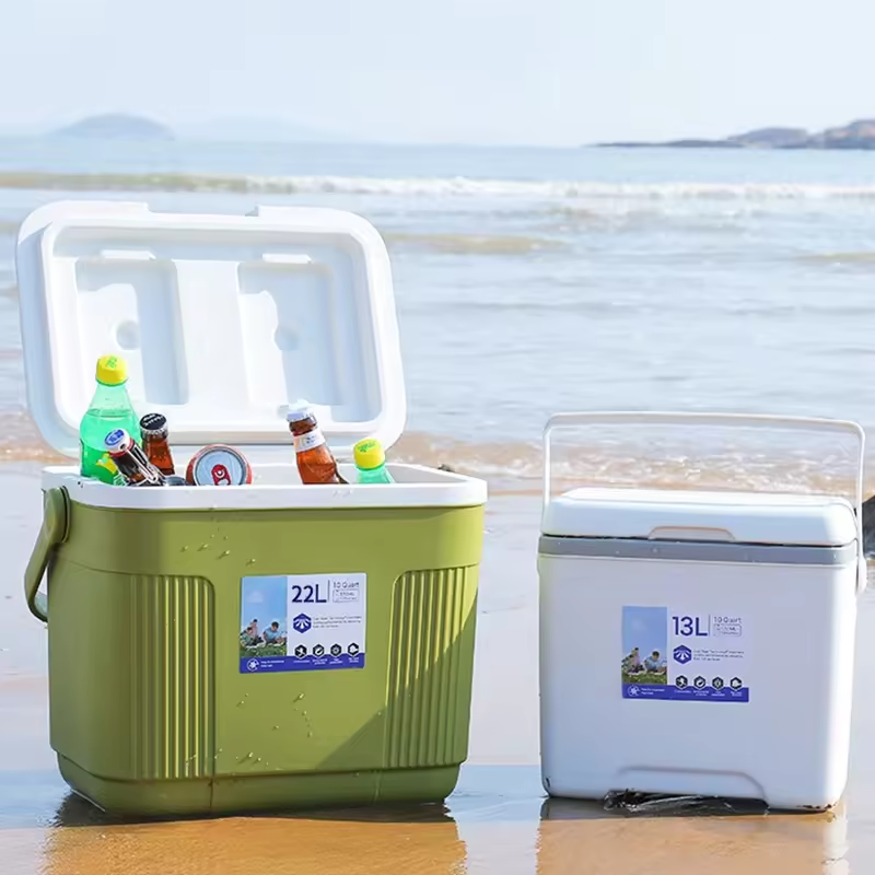 Two portable coolers, one green and one white, placed on a beach with ocean waves in the background. The green cooler has an open lid with bottles inside, and the white cooler is closed.