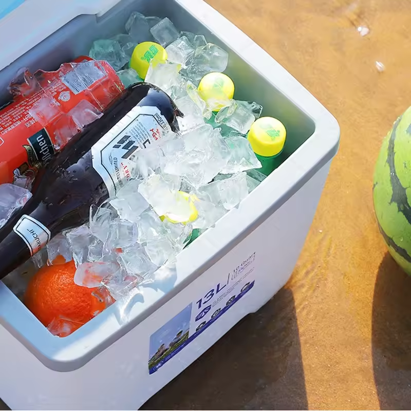 A white cooler filled with ice, containing a soda bottle, a can, and an orange. .