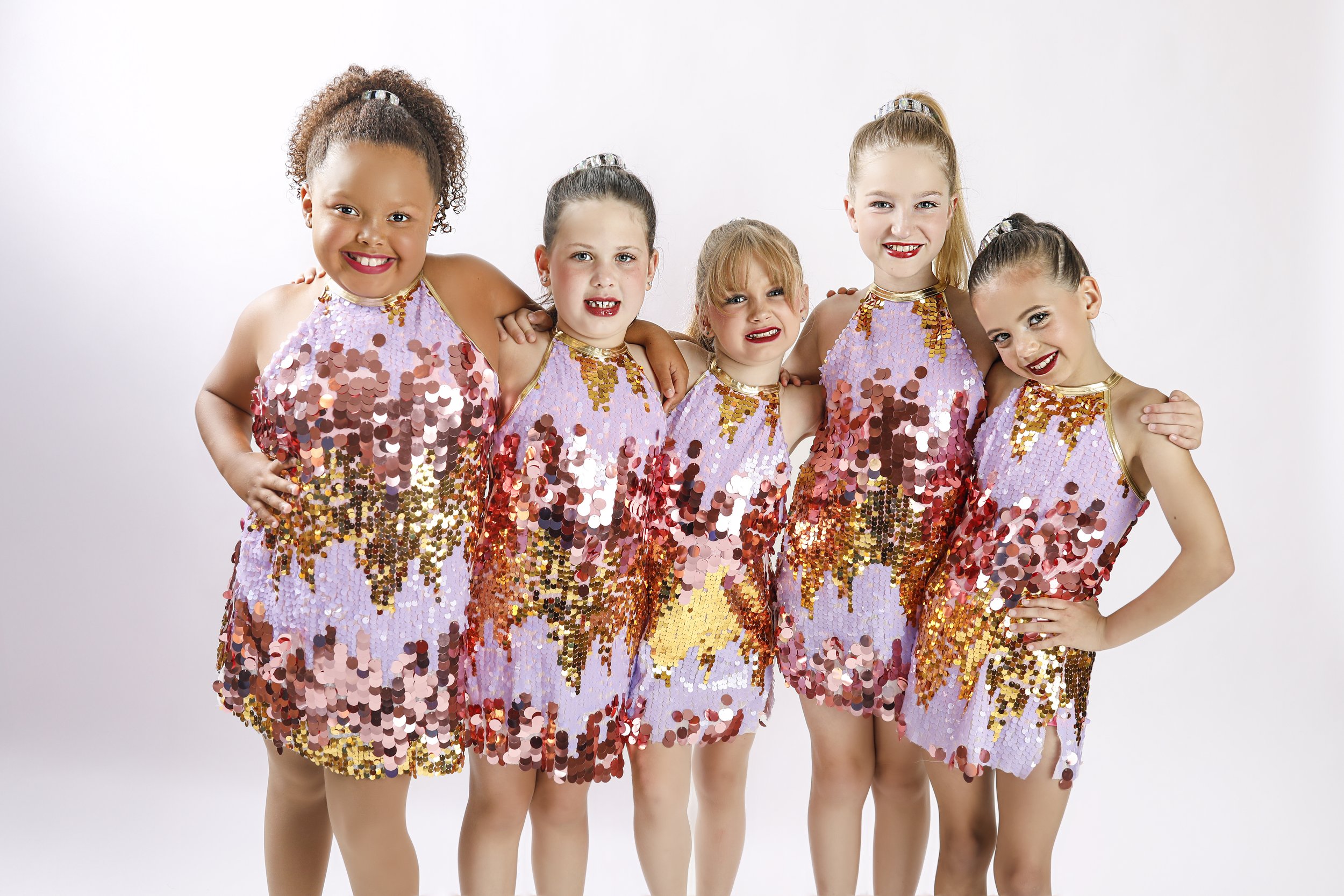 Six young girls in purple sequined costumes, posing together against a white background.