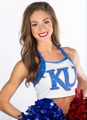Young woman smiling, wearing a KU cheerleading uniform with blue and white colors, holding red and blue pom-poms.