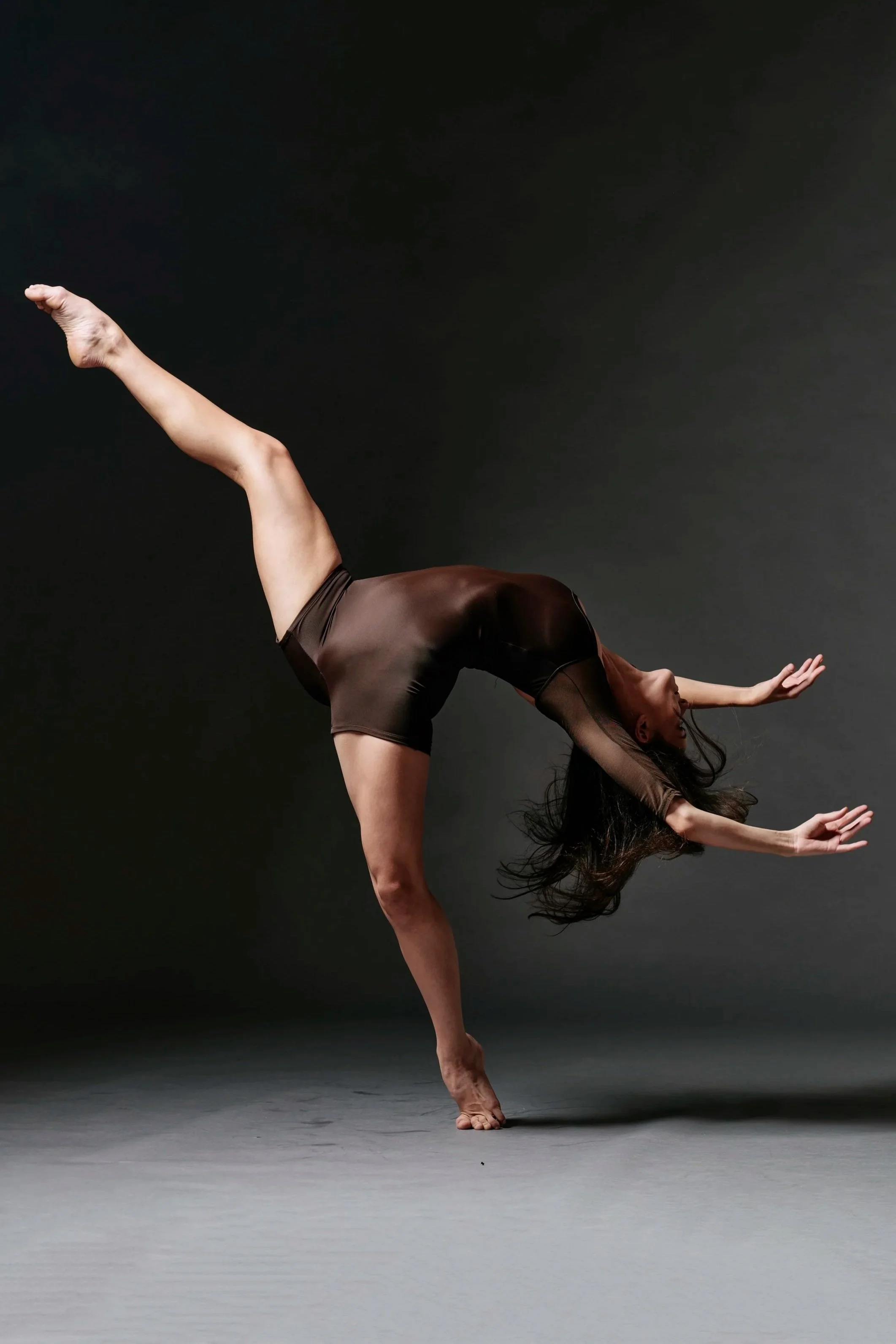 A woman performing a dance move, standing on one leg with the other leg raised behind her, leaning forward with arms extended.