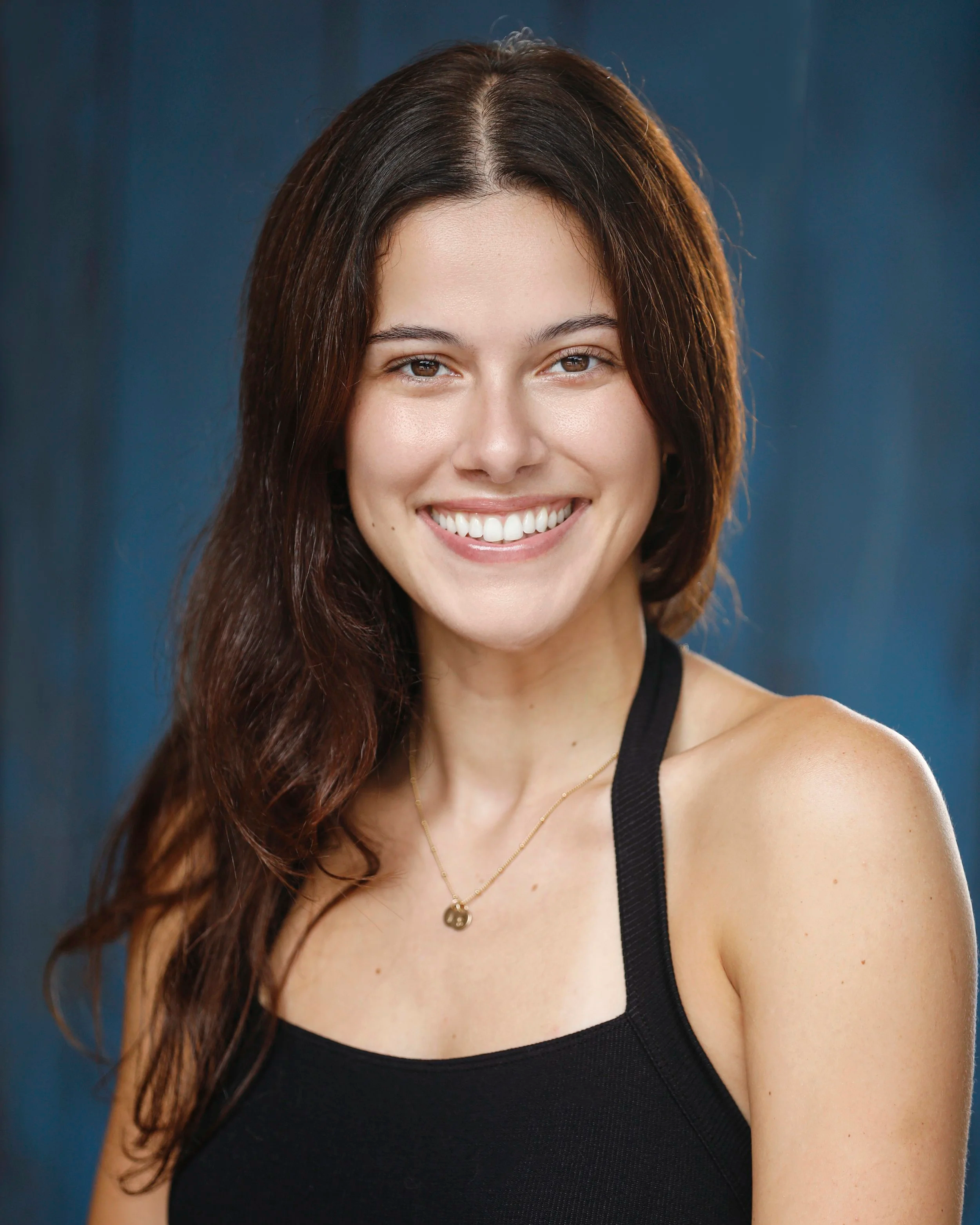 Portrait of a smiling woman with long brown hair, wearing a black tank top and a gold necklace.