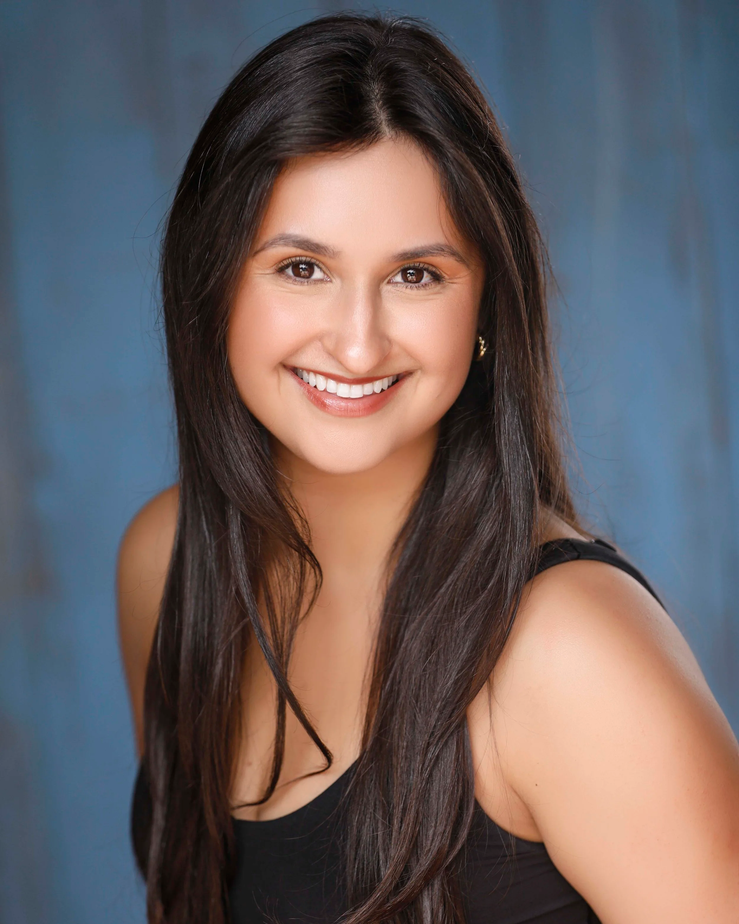 Smiling woman with long dark hair wearing a black top, against a blue background.