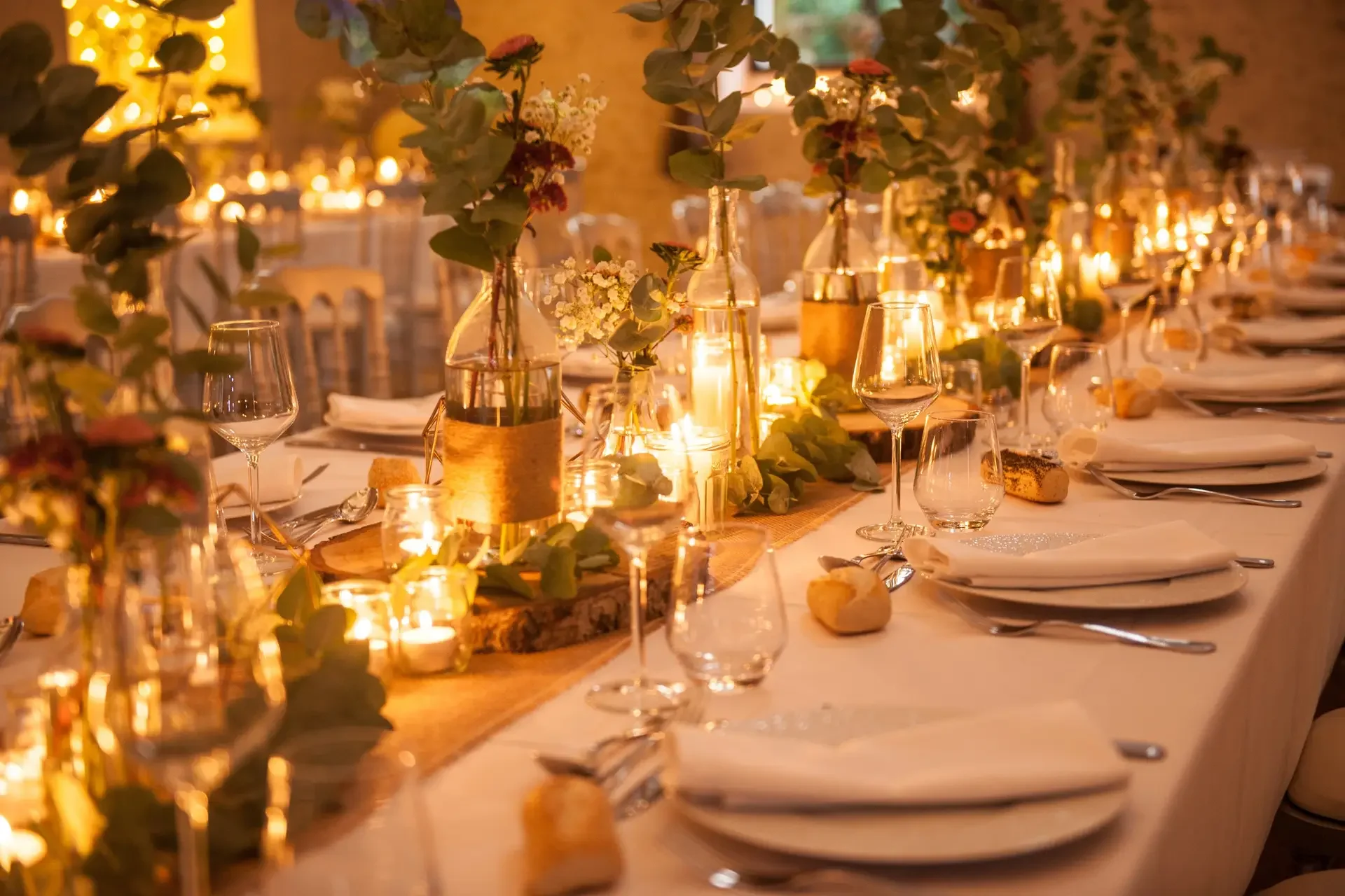 Table dressée pour un dîner de mariage ou une réception, décorée avec des fleurs, des bougies et des verres à vin dans une ambiance chaleureuse et élégante.