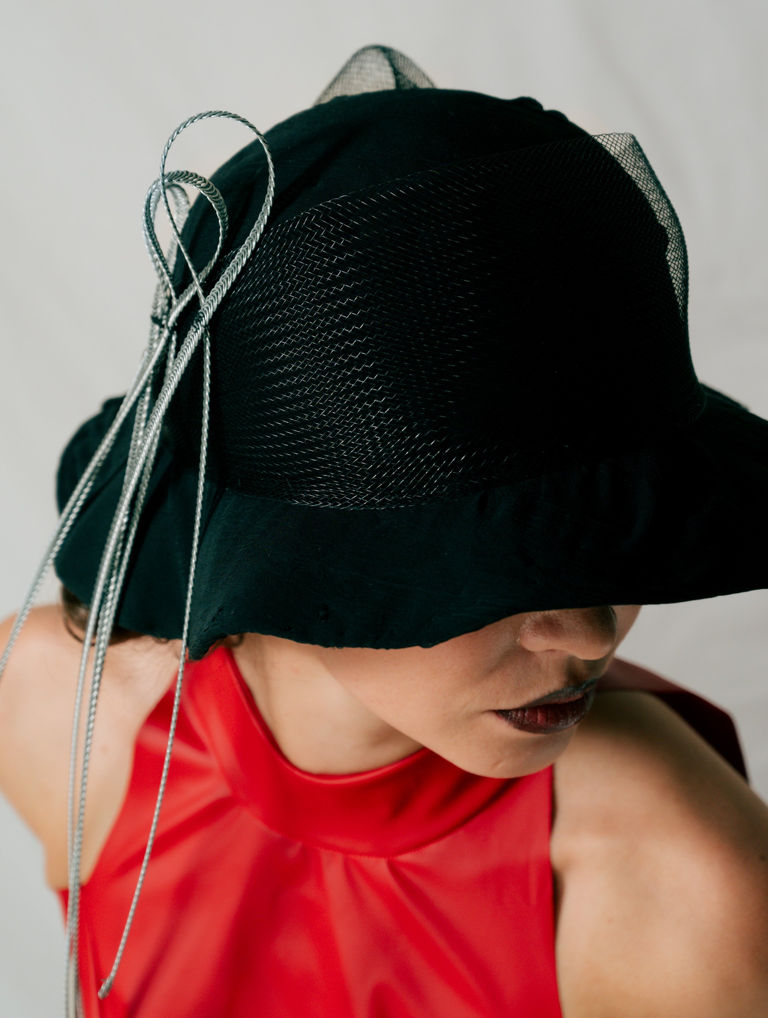 A woman wearing a wide-brimmed black hat with decorative silver cords and a red sleeveless top.