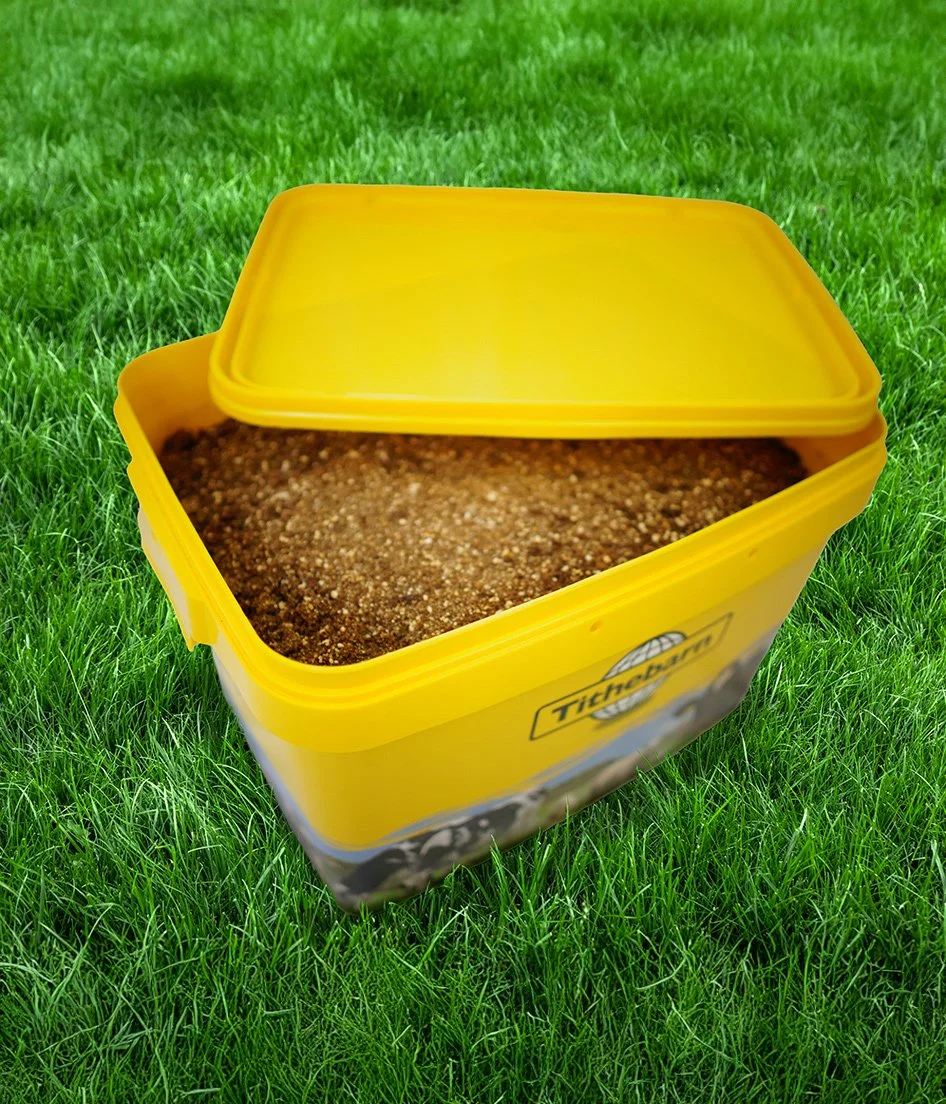 Open yellow plastic bait container with sand or soil inside, placed on green grass.