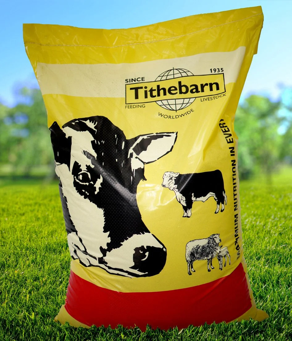 Yellow and red bag of Tithebarn livestock feed with illustrations of a cow, a calf, and a sheep, set outdoors on green grass.
