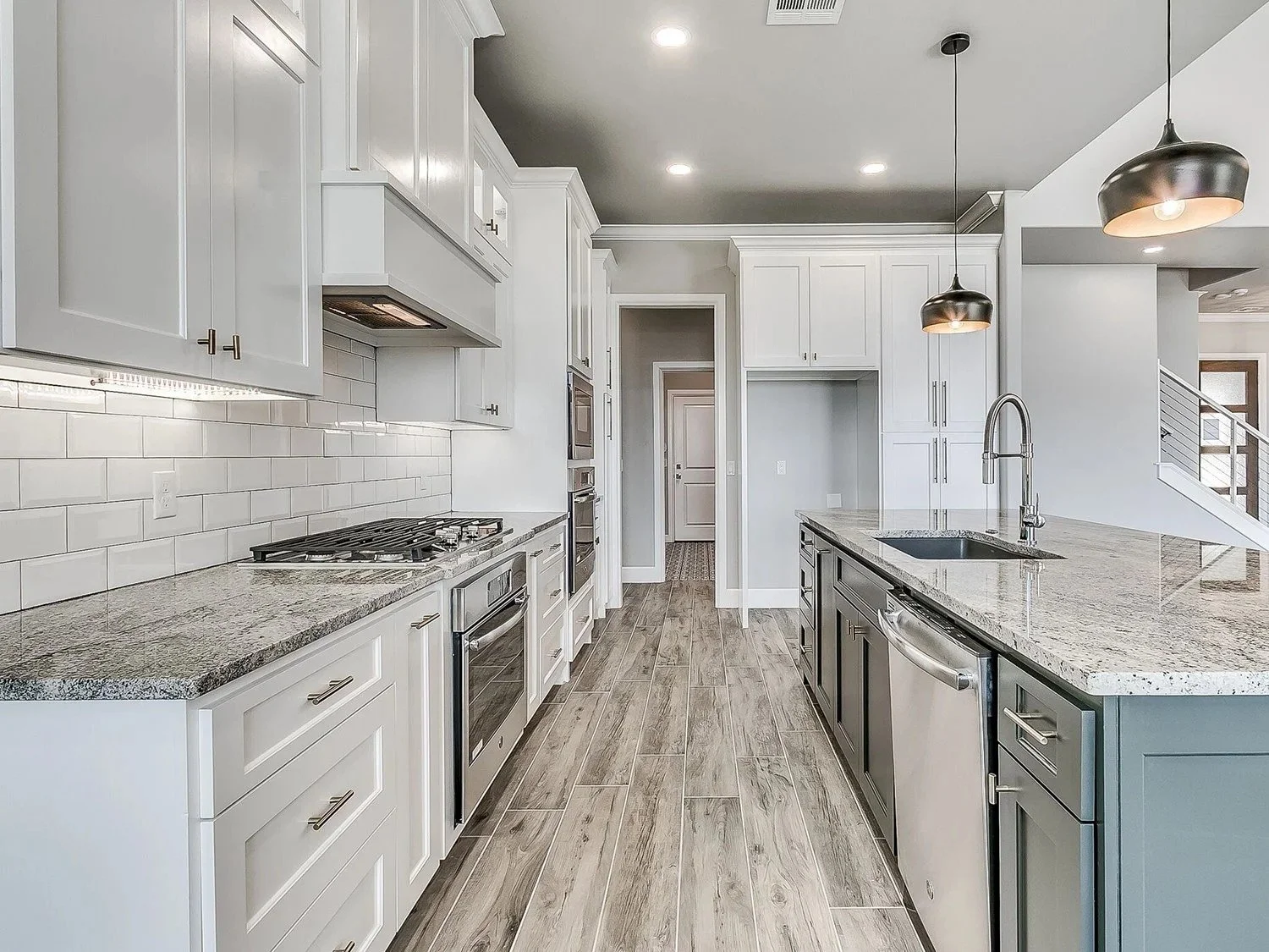 Modern kitchen with white cabinets, stainless steel appliances, granite countertops, pendant lighting, and wood-look tile flooring.