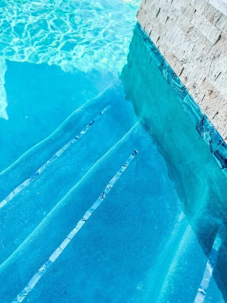 Close-up of blue swimming pool steps with tiled wall beside.