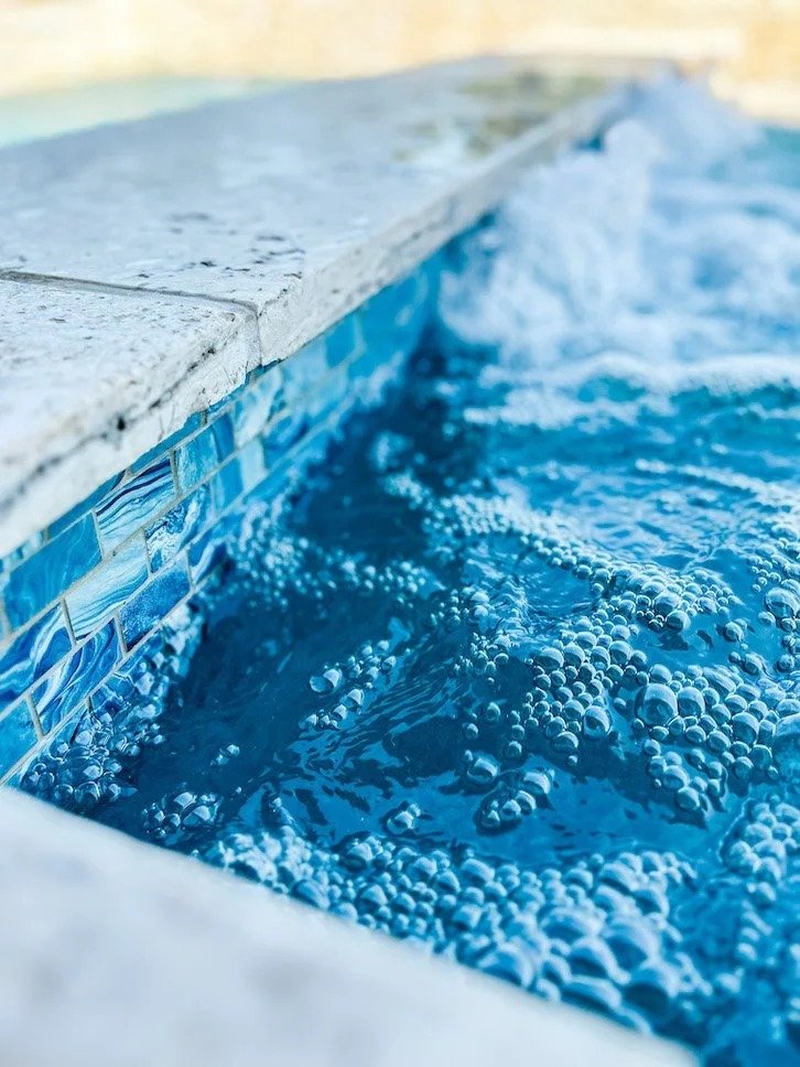 Close-up of the edge of a swimming pool with blue tiles and bubbling water.