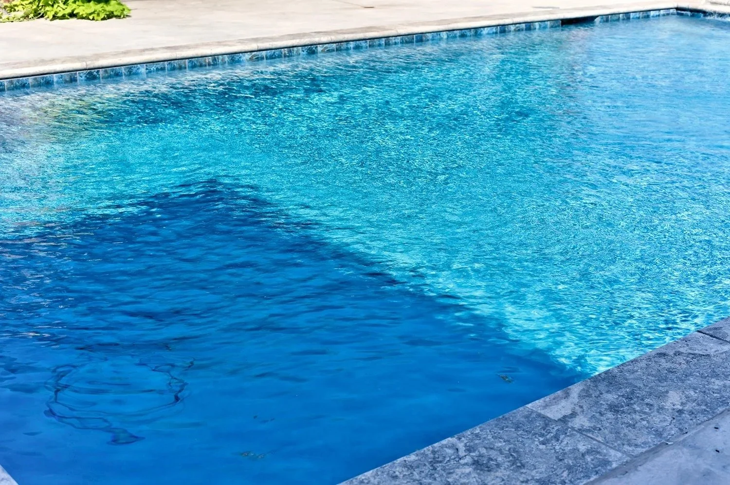Swimming pool with clear blue water and a light-colored concrete pool deck.