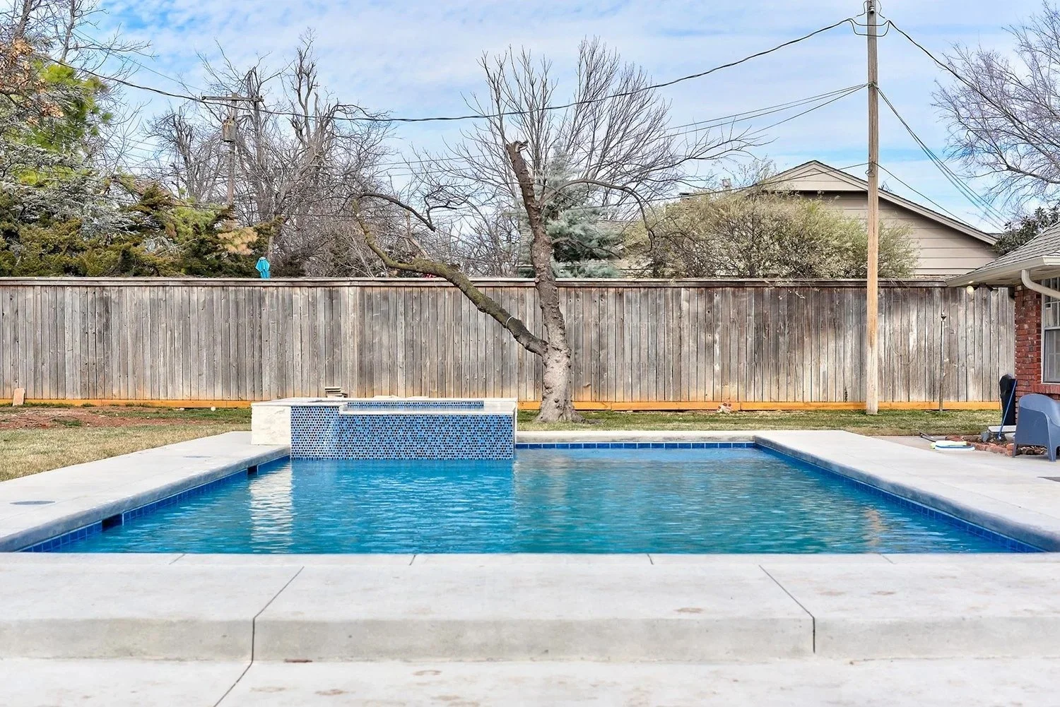 Backyard with a swimming pool, leafless tree, wooden fence, and utility pole with power lines.
