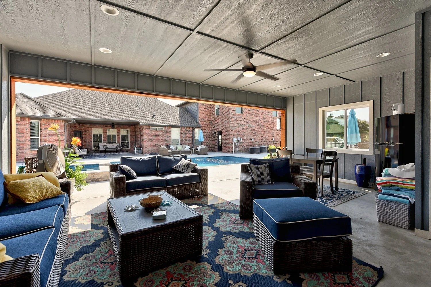 Covered patio area with outdoor furniture overlooking a swimming pool in a backyard.