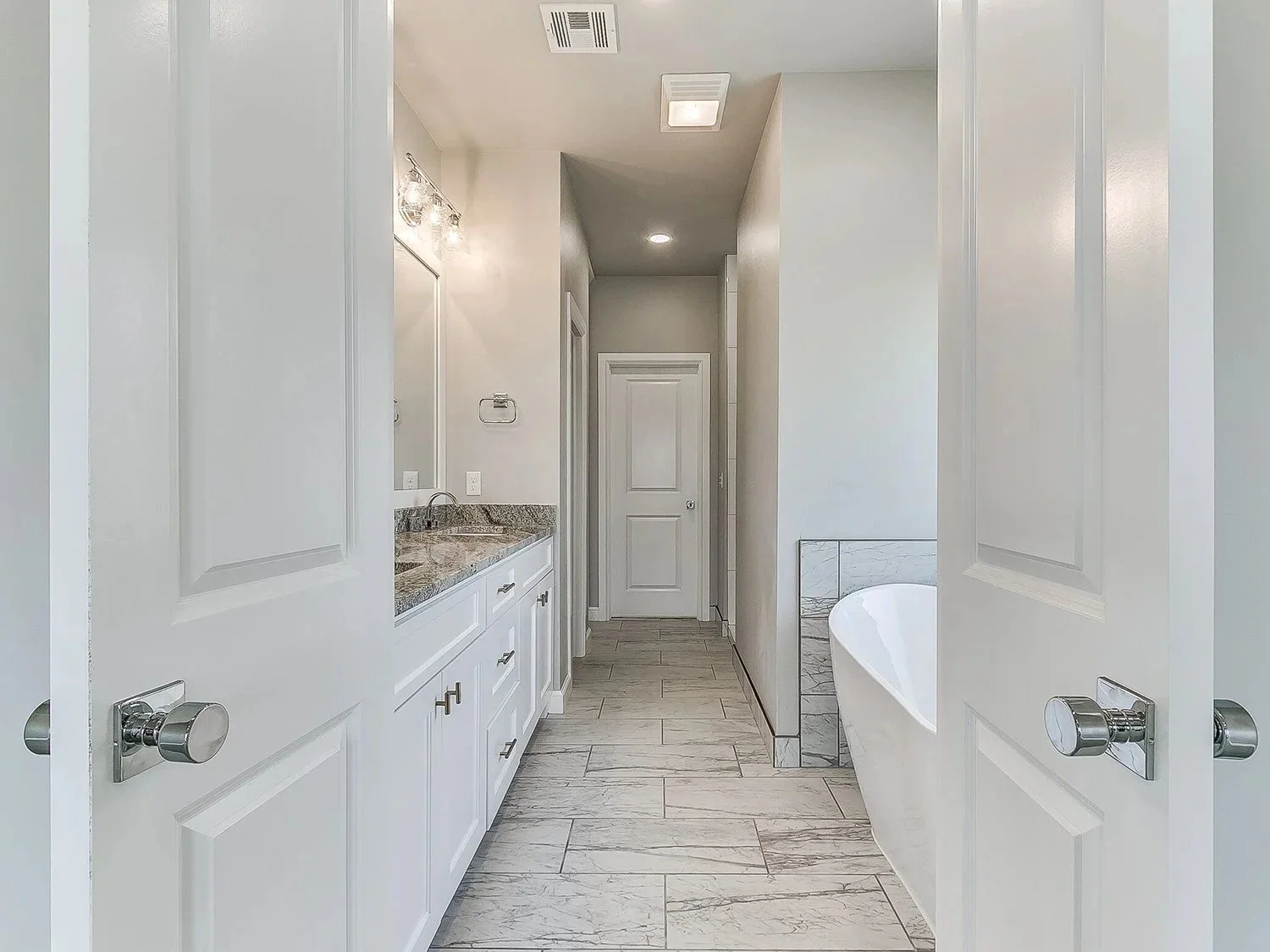 Bathroom with white cabinetry, granite countertop, bathtub, and tiled flooring.