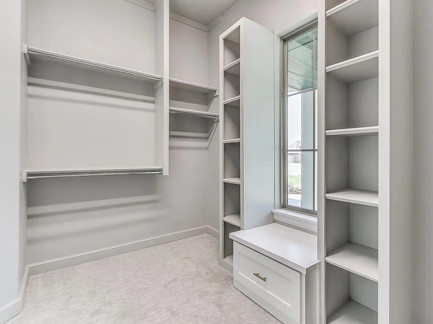 Empty walk-in closet with white shelving, hanging rods, a mirror, and a small bench under the mirror.
