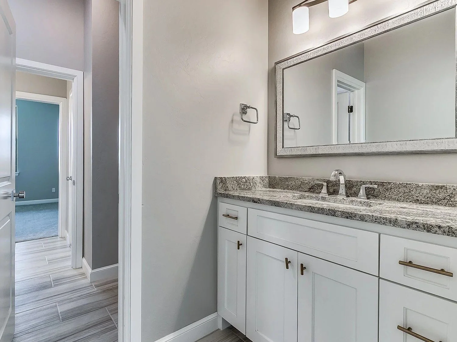 Bathroom vanity with white cabinets, gray granite countertop, and large mirror, with a view into an adjacent room.