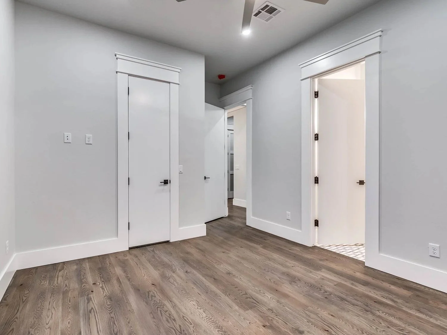 Empty room with light-colored walls, wooden flooring, and several white doors with black handles.