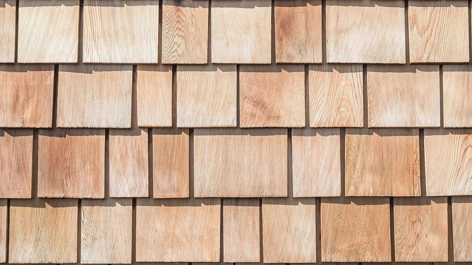Close-up view of a wooden shingle wall with natural-colored square shingles arranged in a grid.