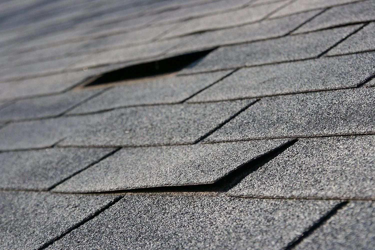 Close-up of a roof with gray asphalt shingles, showing textured surface and some overlapping shingles.