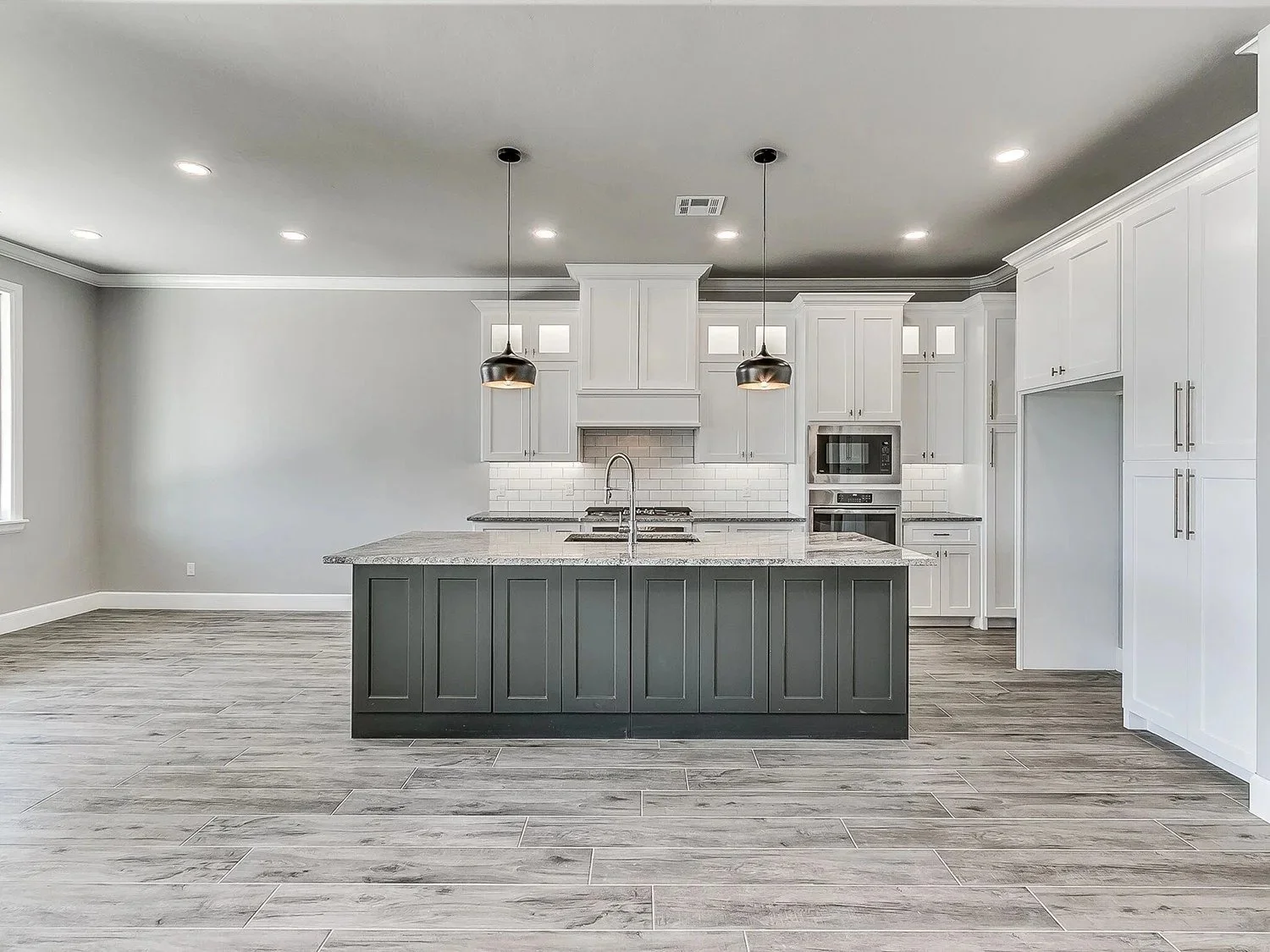 Modern kitchen with white cabinets, a gray island with black panels, granite countertops, and stainless steel appliances.
