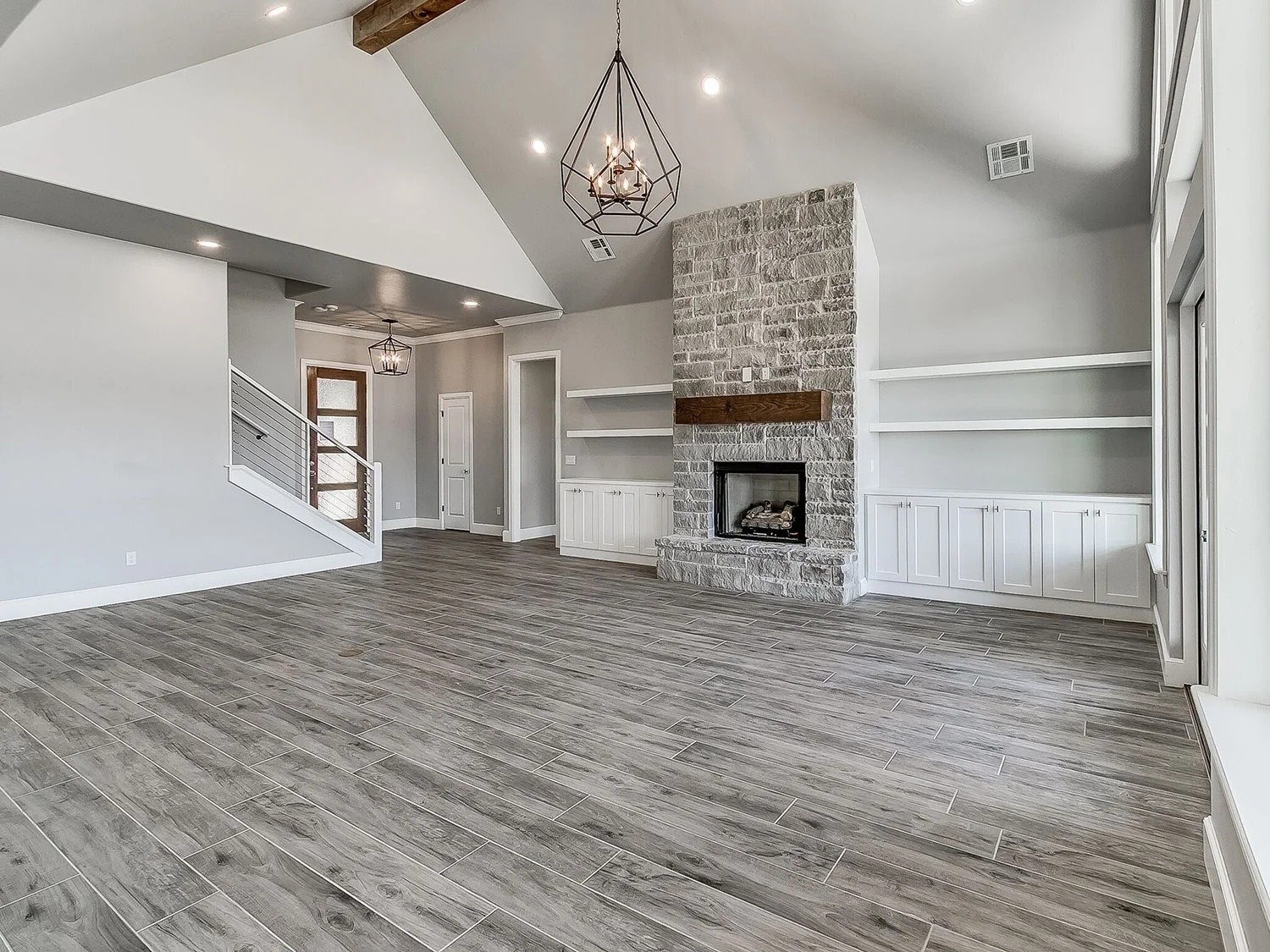 Empty living room with wood-look tile flooring, a brick fireplace, white built-in shelves, and modern lighting fixtures.
