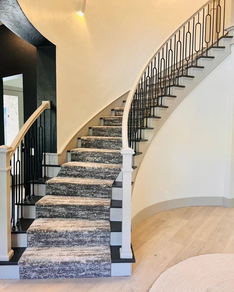 Curved staircase with black metal railing and patterned carpet over wood stairs inside a home.