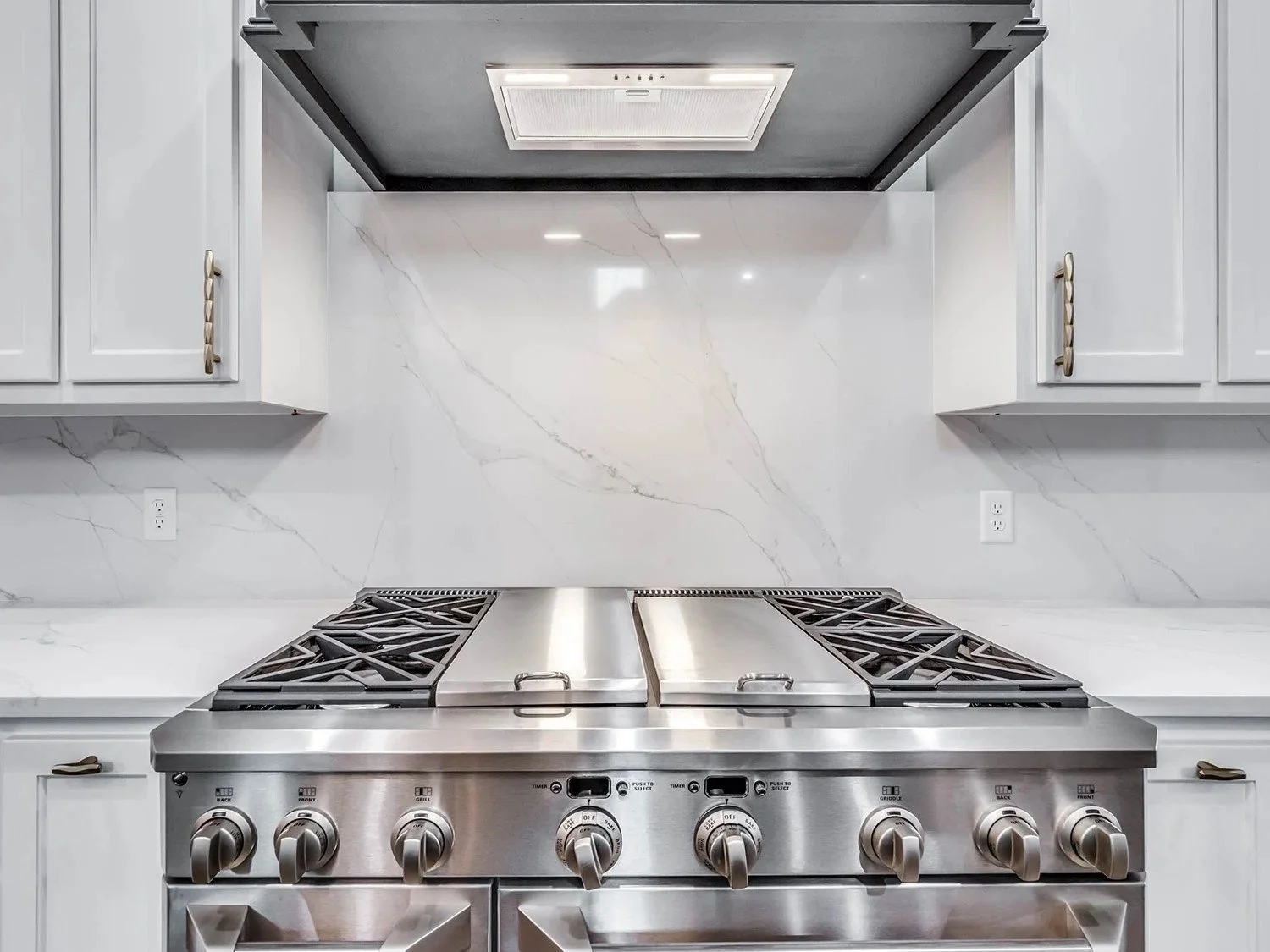 Modern kitchen with stainless steel stove, white marble backsplash, and white cabinets.