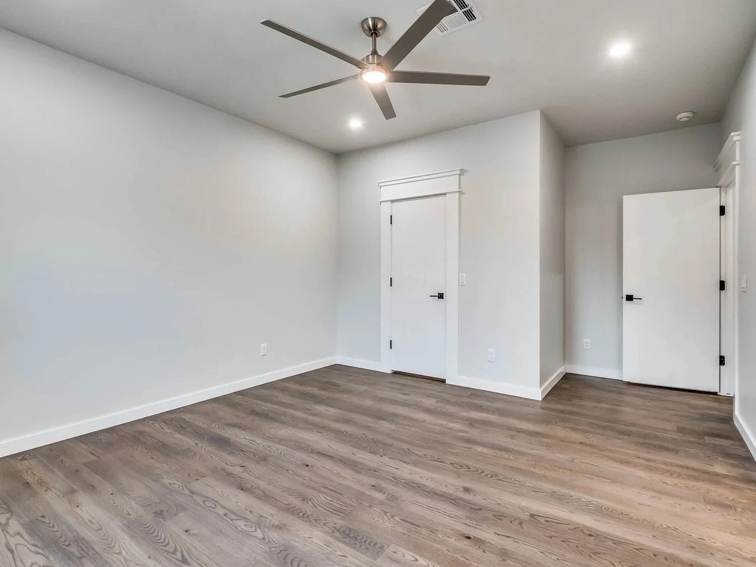 Empty room with white walls, wooden flooring, a ceiling fan, and three doors.