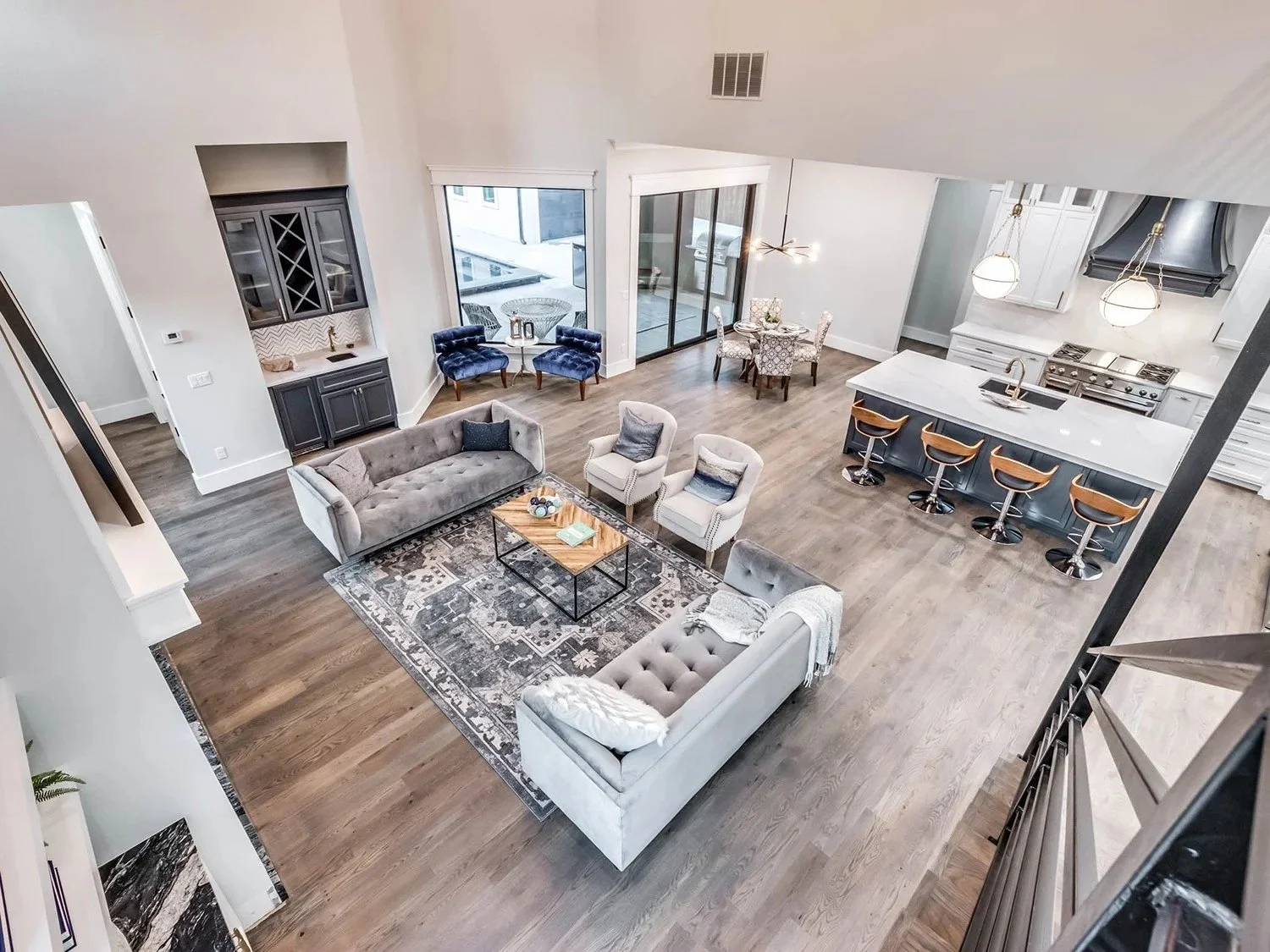 Open-concept living room, kitchen, and dining area in a modern home with hardwood floors, white walls, and large windows.
