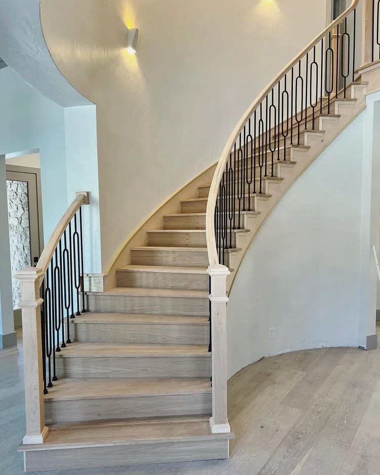 A curved staircase with light wood steps and black metal railing in a modern interior.