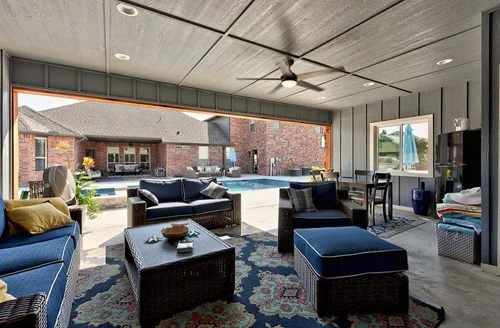 A spacious indoor living room with large sliding glass doors opening to a backyard pool area, featuring patio furniture and house exterior.