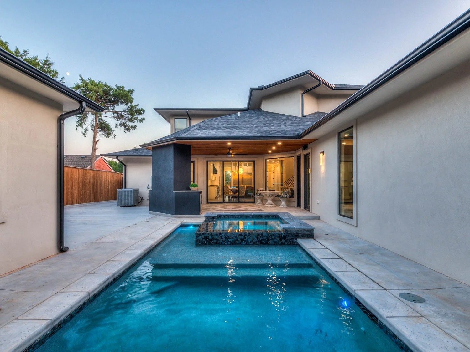 Backyard with a swimming pool, outdoor seating, and a modern house at dusk.