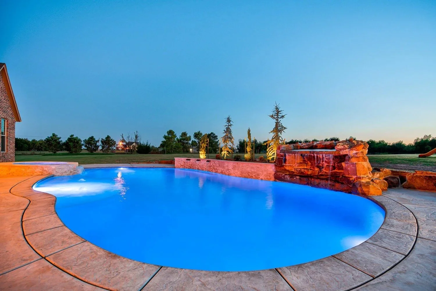Swimming pool with blue water and waterfall feature in backyard during dusk