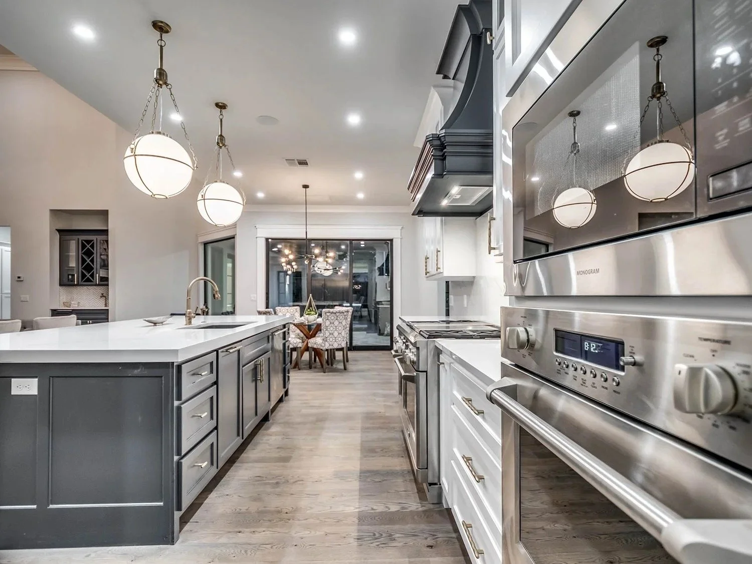 Modern kitchen with stainless steel appliances, gray island, white countertops, and pendant lighting, with a dining area visible in the background.