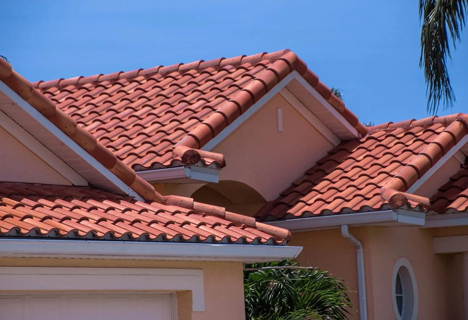 Close-up of a house's pinkish terracotta tile roof with multiple gables and a clear blue sky in the background.