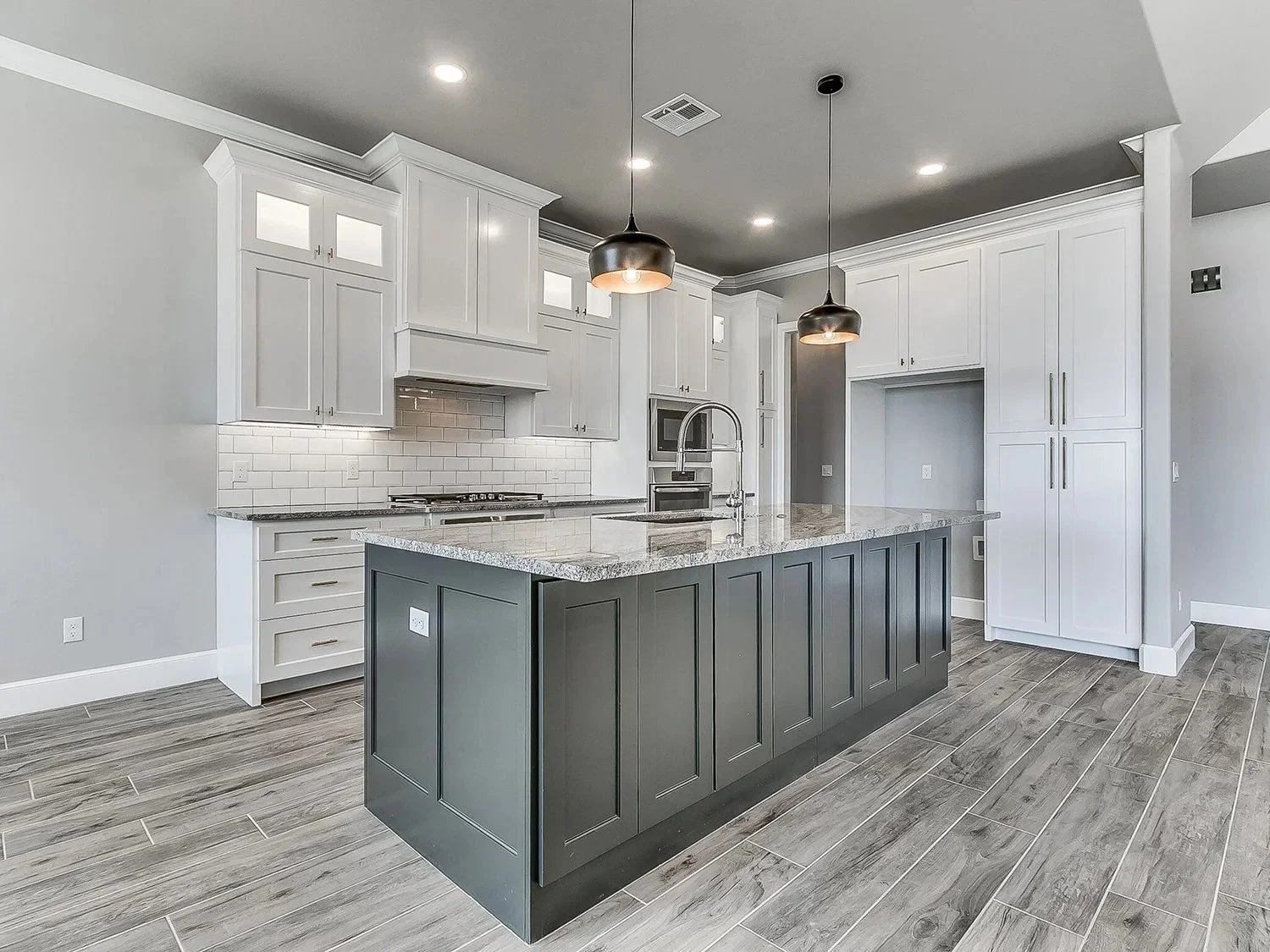 Modern kitchen with white upper cabinets, a gray island, pendant lights, and stainless steel appliances.